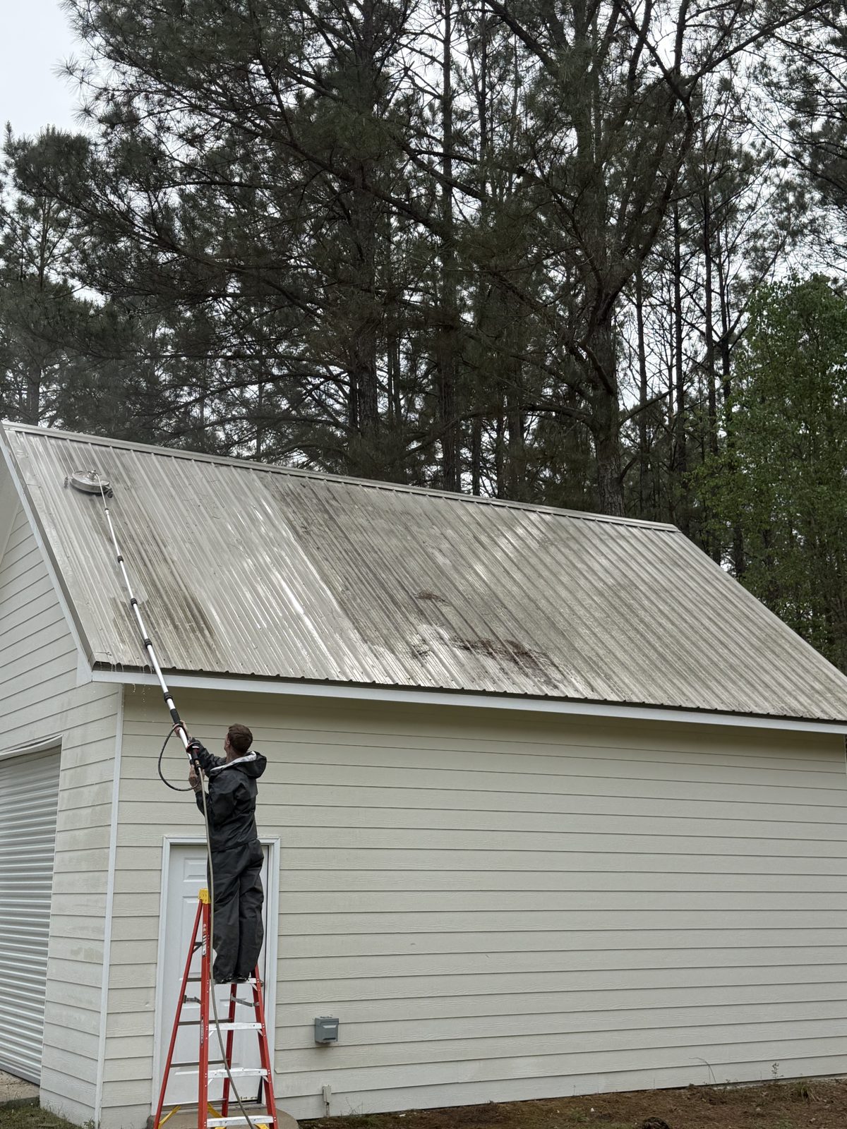 MRA Construction crew member washing a metal shed roof from a ladder